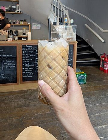 A photo of an iced latte in a glass, held up in a café